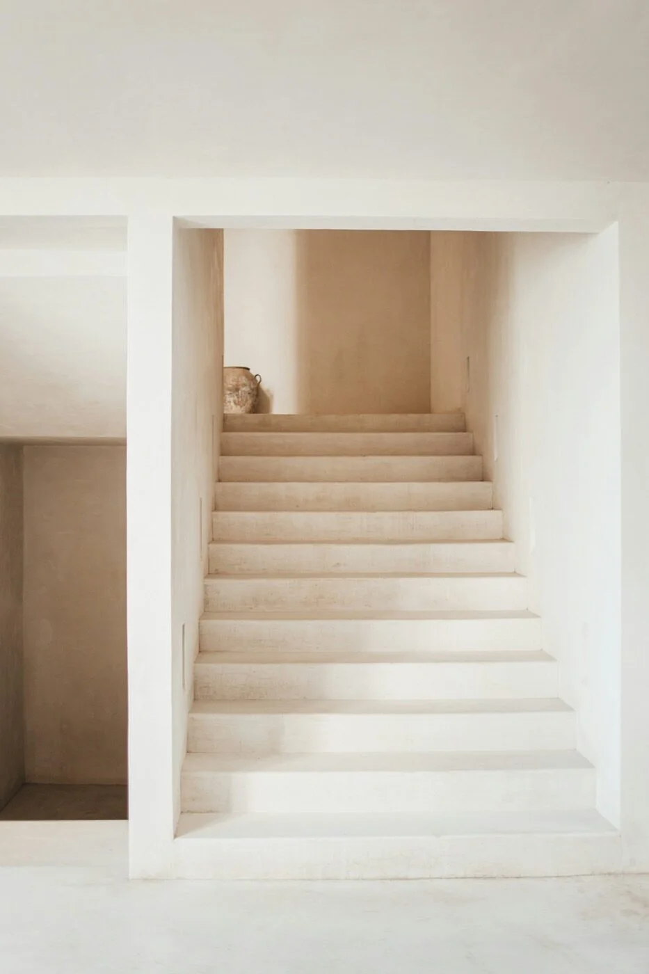 A minimalist plaster staircase in warm white tones with a ceramic vase