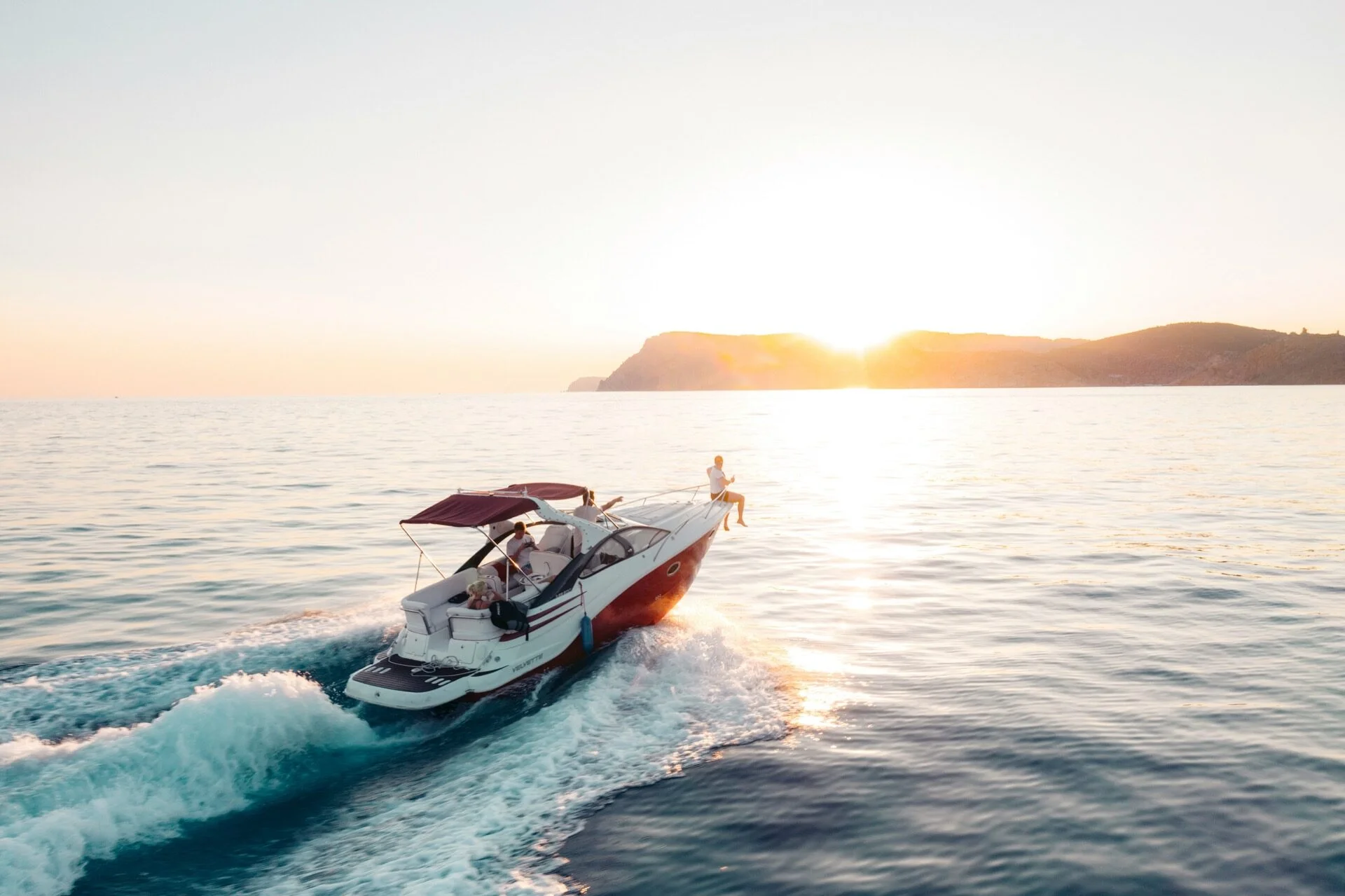 A motorboat cruising past coastal cliffs into a golden-hour sunset